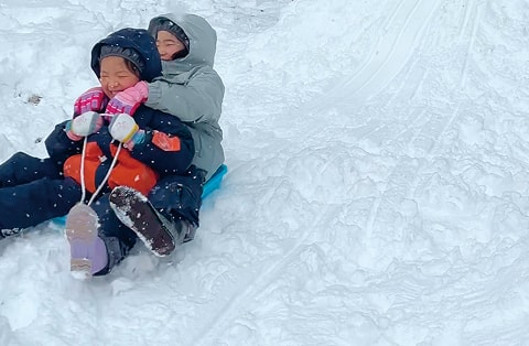 雪の斜面でそり遊びを楽しむ子どもたち
