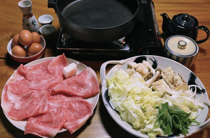 すき焼き用の肉と野菜、卵、鍋が並んだ料理写真